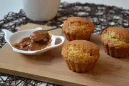 Trzy muffiny z toffifee na desce, obok sos karmelowy w białej miseczce.