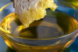 Kawałek chleba zanurzony w oliwie z oliwek w szklanej miseczce.