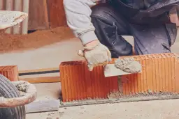 Murarz nakłada zaprawę na pustaki ceramiczne za pomocą kielni.