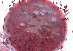 Gęsty, purpurowy mus z czarnej porzeczki, z widocznymi kawałkami owoców i pęcherzykami powietrza, gotowy do podania.