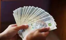 Dłonie trzymają wachlarz banknotów 200 zł. Czy rodzina adopcyjna dostaje pieniądze? To pytanie nurtuje wielu.