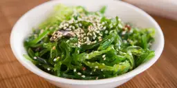 Sałatka z glonów wakame, posypana sezamem, w białej miseczce na bambusowej macie. Idealna na letnie dni.