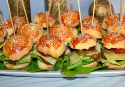 Mini bułeczki do burgerów z sezamem, ułożone na talerzu z sałatą, serem i dodatkami.