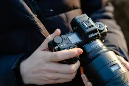 Dłonie trzymają aparat Nikon Z6 III z obiektywem.