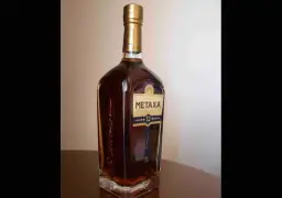Butelka greckiego brandy Metaxa 12 gwiazdek na stole.