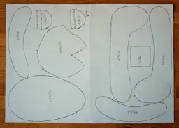 Wzory do wycięcia na papierze, które pomogą Ci dowiedzieć się, jak uszyć misia. Widać części: uszy, ręce, nogi, tułów i łatę.