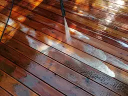 Mycie tarasu wodą pod ciśnieniem to jeden ze sposobów, jak usunąć farbę z drewna domowe sposoby. Woda spływa po deskach.