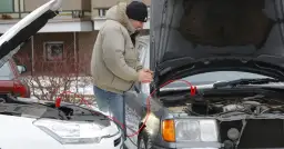 Mężczyzna próbuje odpalić auto zepsutym rozrusznikiem, używając kabli rozruchowych.