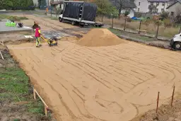 Pracownik zagęszcza piasek zagęszczarką. To kluczowy etap wymiany gruntu pod płytę fundamentową.