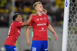 Piłkarze w czerwonych koszulkach świętują bramkę. Jeden z nich, z numerem 18, jest w centrum uwagi, a drugi gratuluje mu, być może to przyszli najlepsi strzelcy ekstraklasy.