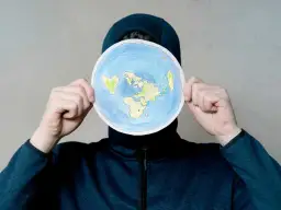 Osoba w kapturze trzyma okrągły rysunek płaskiej Ziemi. To nie jest globe po polsku, ale ciekawa wizja świata.