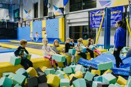 Dzieci bawią się na trampolinach, przygotowując się do urodzin 7 latka. W basenie z gąbkami czeka ich mnóstwo radości.