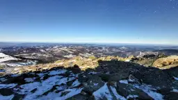 Widok z Babiej Góry zimą. Skaliste szczyty i ośnieżone zbocza Beskidów pod błękitnym niebem.