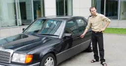 Mężczyzna z kluczykami w dłoni stoi obok czarnego sedana.