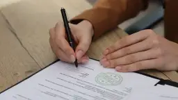 Ręka podpisuje dokument. Uważaj na zapisy, by uniknąć skutków podpisania niekorzystnej umowy wydawniczej.