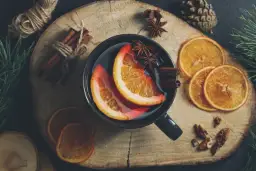 Kubek grzańca z pomarańczą, cynamonem i anyżem na drewnianej desce.