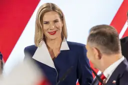 Kobieta w granatowej marynarce z białym kołnierzem uśmiecha się do mężczyzny.