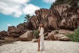 Kobieta w białej narzutce na plaży z granitowymi skałami w tle. Seszele atrakcje to raj dla miłośników przyrody i pięknych krajobrazów.