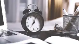 Budzik na biurku obok laptopa i długopisów symbolizuje czas, który upływa, gdy zastanawiamy się, ile trwa rozpatrzenie apelacji.