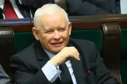 Jarosław Kaczyński w garniturze, siedzi w fotelu, uśmiecha się.