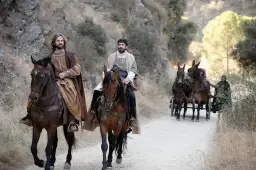 Dwóch mężczyzn na koniach, w tle wóz zaprzężony w muły.