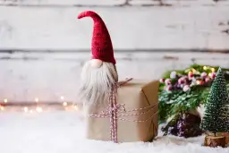 Uroczy skrzat ze skarpety siedzi na prezencie, otoczony zimową scenerią i świątecznymi ozdobami.