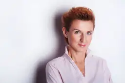 Kobieta z rudymi włosami w jasnoróżowej koszuli, uśmiecha się do obiektywu. Idealne miejsce do robienia zdjęć.