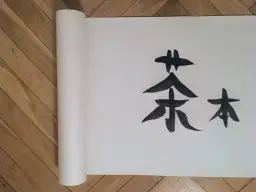 Chiński znak "herbata" namalowany tuszem na zwoju papieru, niczym legenda o herbacie.