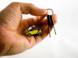 Dłoń trzyma miniaturowy żółty samochód i dwa kluczyki. Zastanawiasz się, ile trwa dorobienie klucza do samochodu?