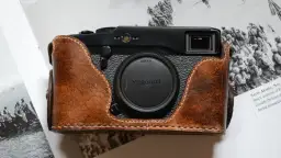 Skórzane etui na aparat Fujifilm X Pro1, z widocznym obiektywem X Mount, leży na stronach książki z historycznymi zdjęciami.