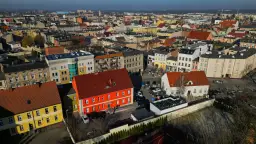 Widok z lotu ptaka na miasto, gdzie leży Ostrów Wielkopolski. Widać kolorowe kamienice, dachy i samochody.