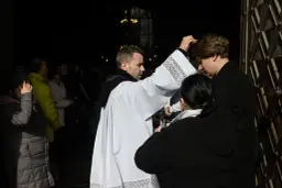 Ksiądz posypuje popiołem głowę wiernego przed kościołem.