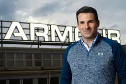Mężczyzna w bluzie Under Armour na tle budynku z napisem ARMOUR.