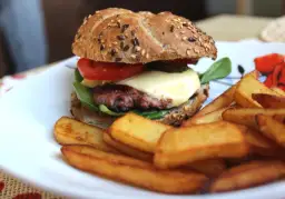 Soczysty domowy burger wołowy z serem, pomidorem i frytkami na talerzu.