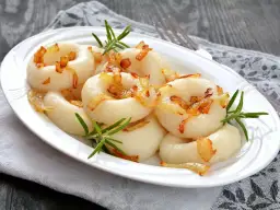 Kluski śląskie z podsmażoną cebulką i rozmarynem na białym talerzu.