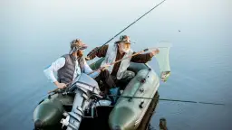 Dwóch wędkarzy w łodzi wyciąga rybę z wody za pomocą podbieraka.