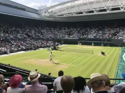 Mecz tenisowy na trawiastym korcie Wimbledonu z widownią na trybunach.