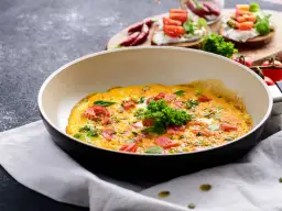 Omlet z pomidorami i ziołami na patelni. Idealny sposób, jak ograniczyć węglowodany w diecie.
