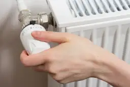 Dłoń reguluje termostat grzejnika.