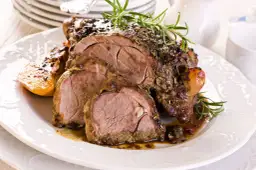 Pieczona baranina z ziołami i pieczonymi warzywami na białym talerzu.