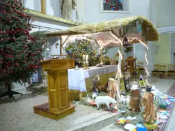 Bożonarodzeniowa szopka i choinka w kościele, ozdobione światłami i figurkami.