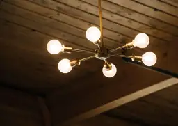 Nowoczesny żyrandol na dwa włączniki, z sześcioma żarówkami, zamontowany na drewnianym suficie.