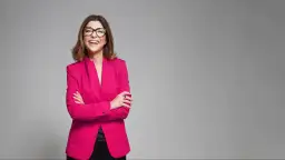 Uśmiechnięta kobieta w różowym żakiecie i okularach, prezentująca styl business formal.