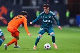 Piłkarz Legii Warszawa z piłką przy nodze, w walce z zawodnikiem Pogoni Szczecin.