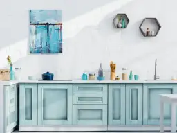 Jasnoniebieskie fronty szafek kuchennych z ozdobnymi ramkami, biała ceglana ściana, obraz i półki.