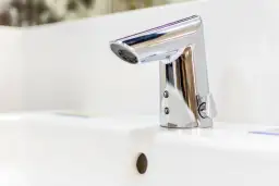 Elegancka bateria umywalkowa z korkiem, wykonana z chromowanego metalu, lśni na białej ceramice.