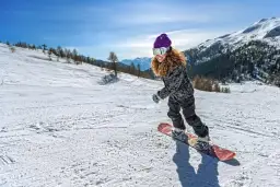 Dziewczyna na snowboardzie, z uśmiechem na twarzy, zjazdem po stoku. Warto wiedzieć, jak ustawić wiązania snowboard, by jazda była bezpieczna i przyjemna.