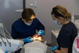 Stomatolog z asystentką w maseczkach wykonują zabieg u pacjentki na fotelu dentystycznym.