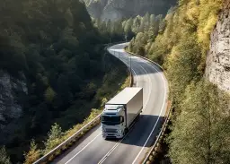 Ciężarówka z naczepą na krętej drodze w górskim krajobrazie.