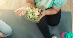 Osoba w stroju sportowym je sałatkę z kurczakiem z plastikowego pojemnika.